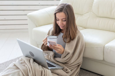 Young woman using phone while sitting on sofa at home