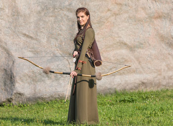 Portrait of woman holding arrow standing against wall