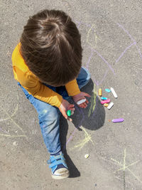 Toddler in jeans draws with crayons on the asphalt . kid's hands are covered with chalks.