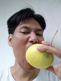 Portrait of man biting yellow fruit against wall