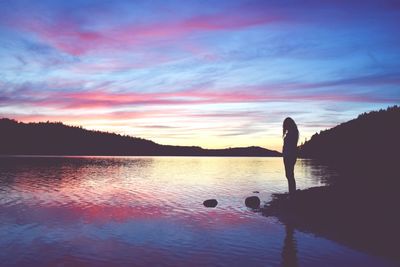 Silhouette woman standing by lake against sky during sunset