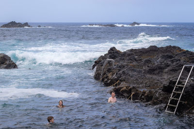 People swimming in natural volcanic thermal sea pool in ponta da ferraria, sao miguel island, azores