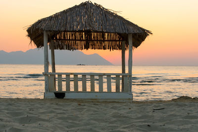 Built structure on beach against sky during sunset