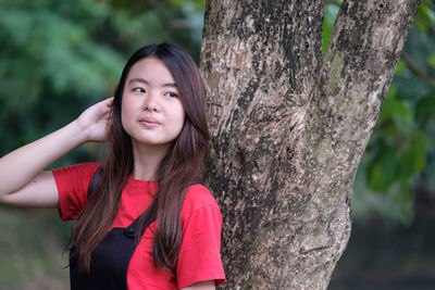 Portrait of smiling young woman against tree trunk