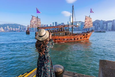 Rear view of woman on sea by city against sky