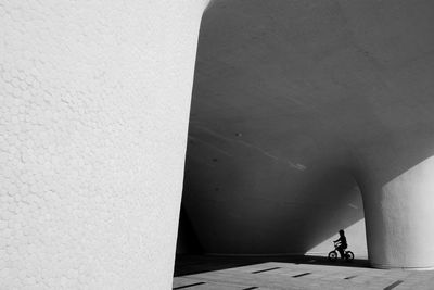 Silhouette child riding bicycle under concrete structure