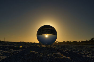 Close-up of crystal ball on land against sky during sunset