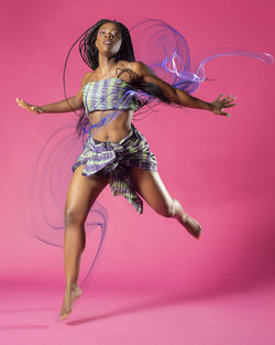 Portrait of young woman dancing against pink background