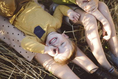 Boy rubbing eye while lying on mother's legs by brother on field