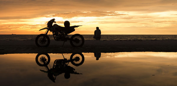 Silhouette of man and motorcycle on beach against sunset sky