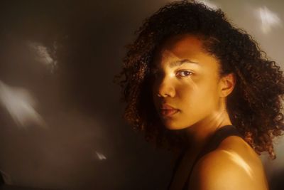 Portrait of beautiful young woman with curly hair against wall