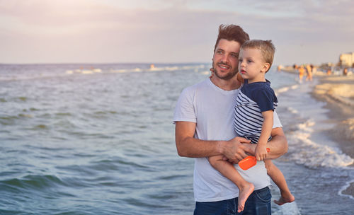 Father carrying cute son while standing at beach