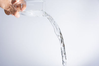 Cropped hand pouring water from glass against gray background