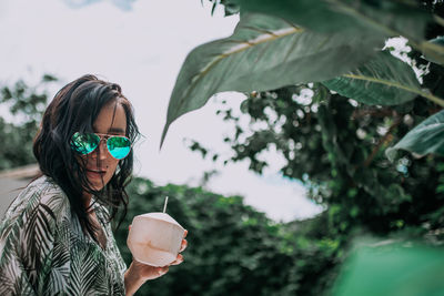 Portrait of young woman wearing sunglasses holding plant