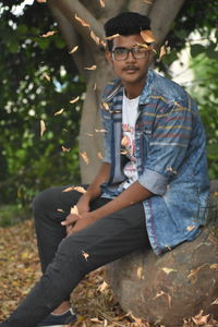 Autumn leaves in mid-air while teenage boy sitting on rock