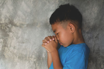 Side view of boy praying by wall