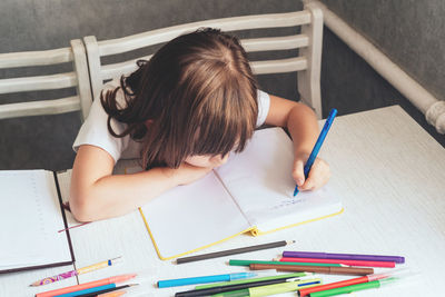 The girl sits at the table and writes with a pen in a notepad.  home education concept