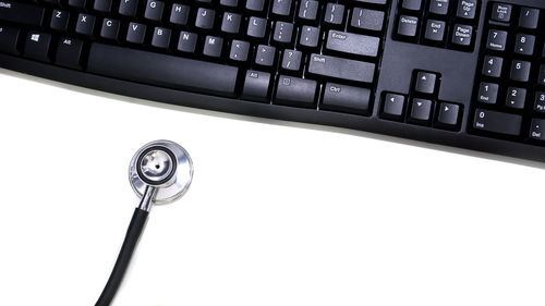 Close-up of stethoscope by computer keyboard over white background