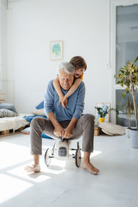 Playful boy with grandfather on toy car in living room at home