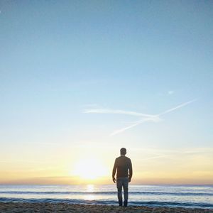 Rear view of silhouette man standing at beach during sunset