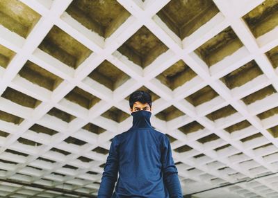 Low angle portrait of confident man covering face with turtleneck t-shirt under bridge