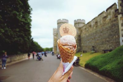 Hand holding ice cream cone against sky and castle fortified walls