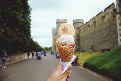 Hand holding ice cream cone against sky