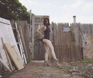 Side view of seductive woman in dress standing against wooden fence