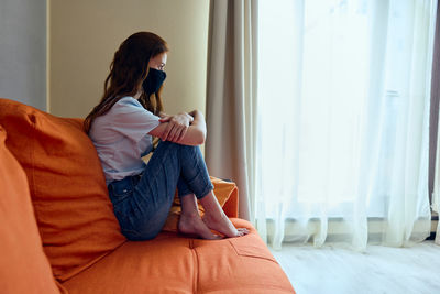 Side view of woman sitting on bed at home