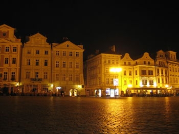Illuminated buildings by street against sky at night