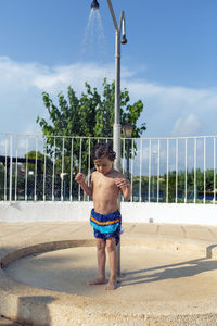 Funny child cooling off in the shower of the swimming pool