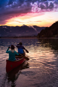 Rear view of people in boat against sky during sunset