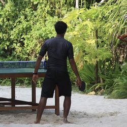 Rear view of man playing table tennis while standing at beach