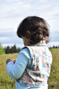 Rear view of little girl standing against sky in field