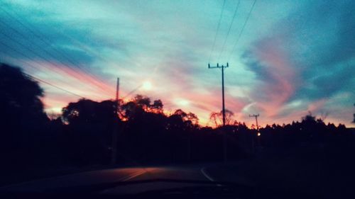 Silhouette trees by road against sky during sunset