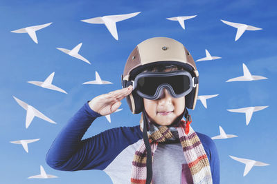 Close-up of boy saluting while standing against blue sky