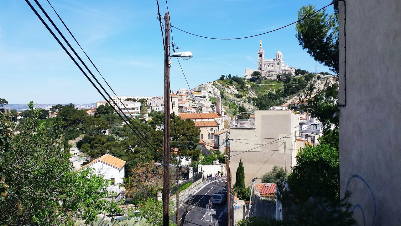 building exterior, architecture, built structure, city, tree, clear sky, power line, residential structure, residential building, house, street, residential district, sky, plant, blue, cable, building, sunlight, growth, electricity pylon