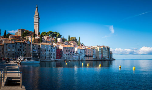 Buildings by sea against blue sky