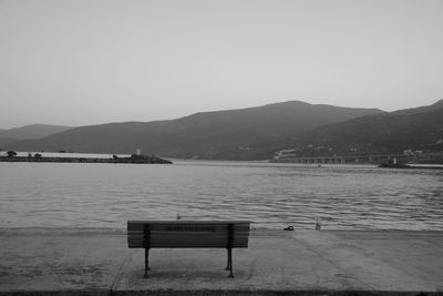 Empty bench in calm sea in front of mountains