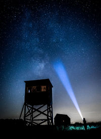 Silhouette woman holding flashlight by tower against star field on land