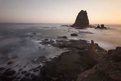 Rocks on beach against sky during sunset