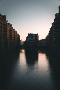 Buildings by river against sky at dusk