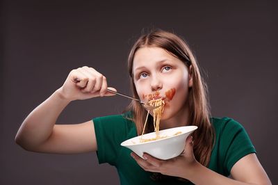 Portrait of young woman eating food against black background