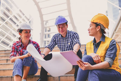 Low angle view of architectures discussing blueprint while sitting on steps