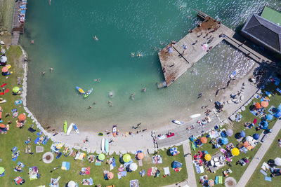 Austria, salzburg, sankt gilgen, aerial view of large group of people sunbathing along sandy shore of lake wolfgang