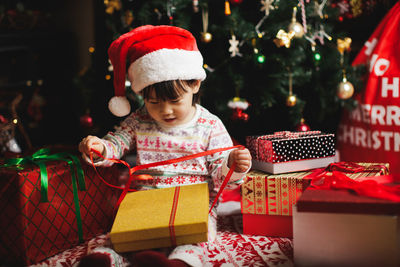 Cute girl opening christmas present against tree at home