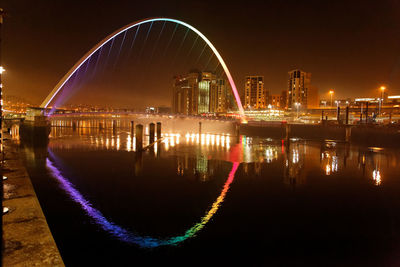 Illuminated bridge over river in city against sky at night