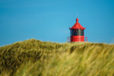 Lighthouse on field against clear blue sky