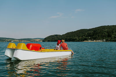 Rear view of man and woman in paddleboat on lake against sky