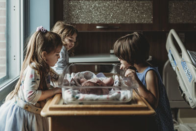 Siblings looking at newborn brother in hospital bassinet